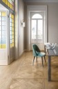 Aranżacja salonu z płytkami Marazzi Intrecci Versailles Miele na podłodze, turkusowe krzesło i białe drzwi balkonowe stanowią stylowe akcenty w klasycznym wnętrzu