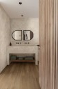 Aranżacja łazienki z płytkami Marazzi Limestone Wall Sand 40x120 cm na ścianie i drewnianą podłogą, dwa okrągłe lustra i drewniane lamele stanowią stylowe akcenty w jasnym wnętrzu