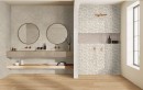 Aranżacja łazienki z płytkami Marazzi Marazzi Limestone Wall Taupe na ścianie i drewnianą podłogą, dwa okrągłe lustra i złoty prysznic stanowią stylowe akcenty w jasnym wnętrzu