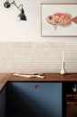Aranżacja kuchni z płytkami Marazzi Limestone Wall Ivory 3D Mikado 40x120 MFCH na ścianie, drewniany blat i obraz z rybą stanowią stylowe akcenty w jasnym wnętrzu
