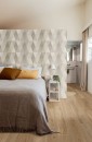 Sypialnia z drewnianą podłogą i beżową pościel, płytki Marazzi Limestone Wall Decoro Losanga Touch na ścianie za łóżkiem tworzą spójną i harmonijną całość