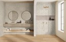 Aranżacja łazienki z wykorzystaniem płytek Marazzi Limestone Wall Decoro Agrifoglio Ivory 40x120 MFCP na ścianie i drewnianą podłogą, dwa okrągłe lustra i złoty prysznic stanowią eleganckie akcenty na tle botanicznego wzoru płytek