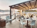 Aranżacja tarasu restauracji z wykorzystaniem płytek Marazzi Market New Limestone Cream na podłodze, białe krzesła i stoły stanowią stylowe akcenty w jasnym wnętrzu z widokiem na jezioro