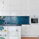 Kuchnia z białymi frontami szafek, drewnianą podłogą oraz niebieskimi płytkami ściennymi - mozaiką dekoracyjną Raw Decor Metropolis Dark Sea