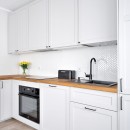 Kuchnia z białymi szafkami, drewnianym blatem, czarną baterią i białymi płytkami ściennymi - mozaiką dekoracyjną Raw Decor Jodełka Biała Połysk z jasną fugą