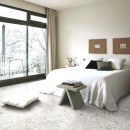 Jasna sypialnia z szarą podłogą wyłożoną płytkami lastryko Marazzi Mystone Ceppo Di Gre White, z dużym oknem i łóżkiem z białą pościelą, przy łóżku stoi szary stolik nocny z książkami, a na ścianie wiszą dwa minimalistyczne obrazy