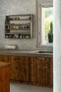 Wnętrze kuchni z jasnoszarą podłogą wykonaną z płytek Marazzi Naturalia Grigio 60x60 cm o subtelnej teksturze prezentuje drewniane szafki z ciemnymi akcentami i szary betonowy blat z wbudowanym zlewem, nad blatem wisi drewniana półka z różnymi pojemnikami