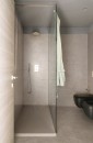 Nowoczesna łazienka z podłogą i ścianami wyłożonymi matowymi, jasnobeżowymi płytkami Marazzi Naturalia Beige 60x120 cm tworzy spójną i spokojną przestrzeń, w pomieszczeniu znajduje się przeszklona kabina prysznicowa oraz czarna toaleta i bidet