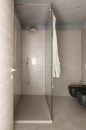 Jasna łazienka, w której beżowe, podłużne płytki Marazzi Naturalia Beige o wymiarach 33x100 MENC pokrywają ściany, nadając im subtelny i nowoczesny wygląd, podłoga również wyłożona jest beżowymi płytkami, a w kadrze widoczny jest prysznic typu walk-in