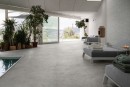 Wnętrze z akcentującą ścianą wyłożoną płytkami Marazzi Naturalia Decoro Classy Grigio Touch 33x100 cm MENK, których subtelny wzór i matowe wykończenie w szarym kolorze tworzą spójną i relaksującą atmosferę w pomieszczeniu z basenem i widokiem na naturę