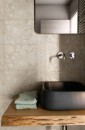 Fragment eleganckiej łazienki, gdzie ściana nad umywalką wyłożona jest beżowymi płytkami Marazzi Naturalia Decoro Incisione Beige Touch 33x100 MENP z subtelnym wzorem kwiatowym, tworzącym delikatne tło dla czarnej, nowoczesnej umywalki i drewnianego blatu