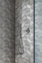 Nowoczesna kabina prysznicowa z bliska, ukazująca ściany pokryte matowymi, szarymi płytkami Marazzi Naturalia Decoro Micro Grigio Touch 33x100 cm MENR, tworzącymi graficzny, trójwymiarowy efekt, widoczna jest chromowana deszczownica i bateria