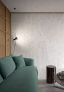 Gresowa, wielkoformatowa, płytka imitująca szary kamień z białymi żyłkami Casalgrande Padana Alabastri White Lucida 120x120 w wysokim połysku na podłodze i ścianie salonu z metalowym okrągłym stolikiem, zieloną kanapą i drewnianą ścianą