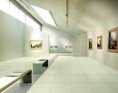 Przestronna, nowoczesna galeria sztuki z jasnymi, beżowymi płytkami podłogowymi Marazzi SistemS Osso 60x60 MQYK, odbijającymi naturalne światło wpadające przez świetliki dachowe i duże okna