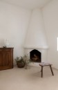 Pokój z narożnym, białym kominkiem i podłogą wyłożoną beżowymi płytkami dekoracyjnymi Marazzi Slow Calce Decoro Rafia 75x75 cm MKGV, tworzącymi subtelny wzór