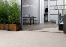Taras z szarymi płytkami antypoślizgowymi imitującymi beton Marazzi Work Beige Outdoor C3 o wymiarach 60x60 cm, otoczony zielenią i nowoczesnymi meblami ogrodowymi