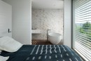 Sypialnia z białymi płytkami strukturalnymi monokolor Marazzi White Deco Strutturato Mikado 60x180 cm MADU na ścianie, tworzącymi subtelny, poziomy wzór, z widokiem na łazienkę z wanną
