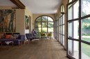 Salon z ciemnobrązowymi płytkami drewnopodobnymi Marazzi Vivo Castano 22,5x180 cm MMD7 na podłodze, z dużymi oknami w kształcie łuków i drzwiami prowadzącymi do ogrodu