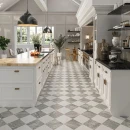 Gresowa płytka podłogowa w szaro białą kamienną szachownicę Realonda Chess Bardiglio 44x44 na podłodze przestronnej klasycznej kuchni. Białe meble uzupełnione o marmurowe i drewniane blaty.