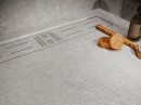 Płytka gresowa, podłogowa w szarym kolorze i matowym wykończeniu, Cifre Acron Pearl Mate N-Plus SI Rect. 60x120, położona w łazience na podłodze pod prysznicem, z odpływem liniowym i drewnianymi dodatkami.