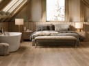 Sypialnia na poddaszu z białą wanną wolnostojącą oraz z drewnopodobnymi płytkami Porcelanosa London Nogal