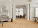 Elegancki salon w stylu glamour ze ścienną sztukaterią, kolumnami, ozdobnym lustrem, jasną sofą i płytkami podłogowymi drewnopodobnymi Porcelanosa London Roble