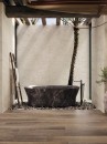 Łazienka z dekoracyjną ścianą, marmurową wanną wolnostojącą oraz płytkami podłogowymi drewnopodobnymi Porcelanosa Bruselas Walnut