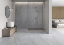 Gresowe szare płytki imitujące kamień Pamesa Kenzo Blanco Satin 90x90 na ścianie otwartej łazienki połączonej z sypialnią. Złota armatura łazienkowa, wykończenia w brązowym kolorze.