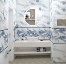 Płytka ścienna imitująca marmur w kolorze biało niebieskim, wykończenie powierzchni strukturalne w połysku, Geotiles RLV Valeria Blue 25x50, położona na ścianie w łazience z białą armaturą oraz okrągłym wiszącym lustrem