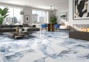 Płytka gresowa, podłogowa imitująca biały marmur, wykończenie powierzchni w połysku. Geotiles Valeria Blue Rect. 60x120, położona na podłodze w dużym salonie z szarym wypoczynkiem, obrazami oraz oknami z widokiem na centrum