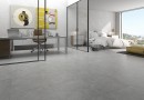 Płyta gresowa, podłogowa w kolorze szarym, wykończenie powierzchni matowe, Geotiles Sena Gris Natural 60,8x60,8 położona na podłodze w sypialni z dużym łóżkiem oraz oknem z widokiem na miasto, oraz w gabinecie z biurkiem