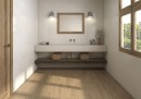 Beżowa gresowa płytka imitująca beton Pamesa Coralstone Marfil Satin 90x90 na ścianach łazienki w zestawieniu z drewnem na podłodze oraz drewnianymi drzwiami i ramą w oknie