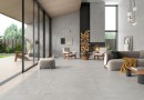 Płytka gresowa, podłogowa w kolorze szarym, wykończenie powierzchni matowe, Geotiles Argon Perla Natural 45x45, położone na podłodze w salonie, w którym znajduje się kominek a przy nim dwa fotele, jasny wypoczynek oraz brązowy stół