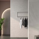 Płytka gresowa, podłogowa w szarym kolorze imitująca kamień, wykończenie powierzchni matowe, Geotiles Eddystone Perla Mate 60,8x60,8 położona na ścianie w pomieszczeniu gdzie znajduje się kwiatek ozdobny oraz wieszaki z ubraniami
