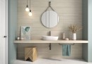 Płytka ścienna imitująca drewno w kolorze beżowym, wykończenie powierzchni matowe strukturalne, Geotiles Haru RLV Almond 31,6x60 położona na ścianie w łazience gdzie znajduje się umywalka, wiszące lustro, drewniany taboret oraz wisząca lampa