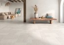 Płytka gresowa, podłogowa w kolorze białym, wykończenie powierzchni matowe strukturalne, Geotiles Montpellier RLV Blanco Matt Rect. 60x120 położona na podłodze w pokoju gdzie znajduje się wypoczynek w jasnym kolorze, lampa wisząca oraz stolik na kwiaty