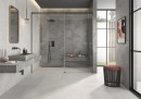 Płytka gresowa, podłogowa w kolorze szarym, wykończenie powierzchni matowe, Geotiles Hermes Perla 60,8x60,8 położona na ścianie w łazience gdzie znajduje się duży prysznic, umywalka oraz prostokątne wiszące lustro