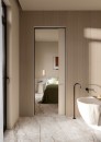 Elegancka łazienka oddzielona od sypialni drzwiami, ściany łazienki wykończone beżowymi, trójwymiarowymi płytkami Marazzi Crea Forma01 3D Rovere Scuro 60x135 cm MQDW z efektem pionowego, gęstego ryflowania, na podłodze widoczne są płytki imitujące marmur