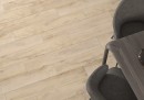 Płytka gresowa, podłogowa imitująca drewno w kolorze beżowym, wykończenie powierzchni matowe, Cerrad Guardian Wood Light Beige 19,3x120,2, położona na podłodze, gdzie znajduje się ciemny stolik oraz dwa ciemne krzesła