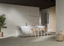 Płytka gresowa, podłogowa imitująca kamień w kolorze szarym, wykończenie powierzchni matowe, Cerrad Softstone Pearl Rect. 59,7x59,7 położona w pomieszczeniu na ścianie gdzie znajdują się krzesła, kwiatek oraz wyspa kuchenna
