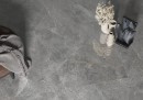 Płytka gresowa, podłogowa imitująca kamień w kolorze grafitowym, wykończenie powierzchni satynowe, Cerrad Distinct Grey Silky Cristal 59,7x119,7 położona na podłodze gdzie znajduje się taboret oraz wazon na kwiaty i rzeźba
