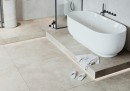 Płytka gresowa, podłogowa imitująca beton w kolorze szarym, wykończenie powierzchni matowe, Cerrad Tacoma Silver Rett. 59,7x59,7 położona na podłodze w łazience gdzie znajduje się duża biała wanna oraz prysznic w rogu łazienki
