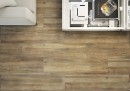 Płytka gresowa, podłogowa imitująca beton w kolorze brązowym, wykończenie powierzchni matowe, Cerrad Mattina Marrone Rect. 19,3x120,2 położona na podłodze w salonie gdzie znajduje się jasna kanapa oraz przeszklony stolik