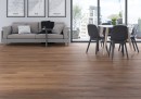 Płytka gresowa, podłogowa imitująca drewno w kolorze brązowym, wykończenie powierzchni matowe, Cerrad Tonella Honey 19,3x120,2 położona na podłodze w salonie gdzie znajduje się wypoczynek, stół z krzesłami oraz okno z widokiem na miasto