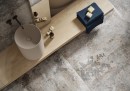 Płytka gresowa, podłogowa imitująca beton w szarym kolorze, wykończenie powierzchni lappato, Cerrad Endless Time Rust Silky Cristal Lappato Rect. 59,7x59,7 położona na podłodze w łazience gdzie znajduje się umywalka z lustrem