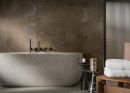Płytka gresowa, podłogowa imitująca kamień w brązowym kolorze, wykończenie powierzchni matowe, Cerrad Softstone Brown Rect. 59,7x59,7 położona na ścianie w łazience gdzie znajduje się duża biała wanna oraz stolik na kosmetyki i ręczniki