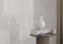Płytka gresowa, podłogowa imitująca beton w kolorze szarym, wykończenie powierzchni satynowe, Cerrad Textural White Silky Cristal 59,7x59,7 położona na ścianie w pomieszczeniu gdzie znajduje się stolik z książkami oraz wazonem