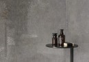 Płytka gresowa, podłogowa imitująca beton w kolorze szarym, wykończenie powierzchni matowe, Cerrad Textural Grey Silky Cristal 59,7x59,7 położona na ścianie w pomieszczeniu gdzie znajduje się stolik w czarnym kolorze z kosmetykami