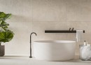 Płytka gresowa, podłogowa imitująca kamień, wykończenie powierzchni matowe, Cerrad Softstone Ivory Rect. 59,7x119,7 położona na ścianie w łazience gdzie znajduje się biała wanna, półka na kosmetyki oraz roślina ozdobna
