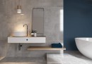 Płytka gresowa, podłogowa imitująca beton, wykończenie powierzchni matowe, Cerrad Softcement Silver Rect. 59,7x59,7 położone na ścianie w łazience gdzie znajduje się biała wanna, umywalka oraz lustro